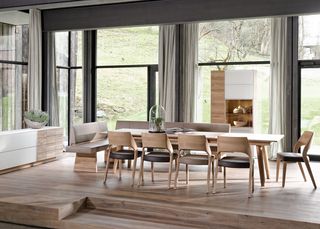 langer Holztisch mit Holzstühlen mit hellbrauner Ledersitzfläsche vor weißem Sideboard und Holzschrank
