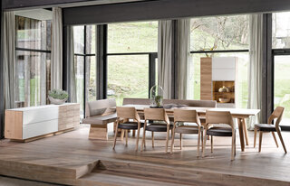 langer Holztisch mit Holzstühlen mit hellbrauner Ledersitzfläsche vor weißem Sideboard und Holzschrank