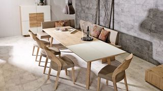 Heller Holztisch mit zum Teil weißer Platte mit beigen Sitzbänken und Stühlen aus Leder vor weißem Sideboard mit Holz