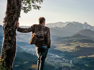 Mann lehnt sich mit den Arm an Baum und sieht auf Landschaftspanorama