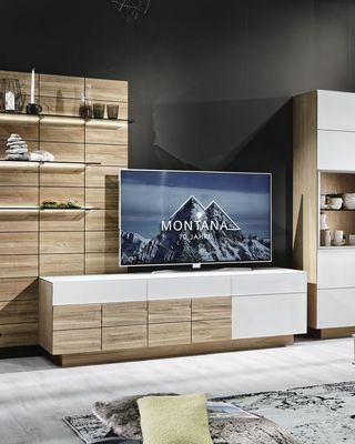 Dunkles Sofa und Teppisch vor Holzwohnwand mit grauem Hängeelement und Fernseher