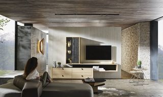 Frau sitzt im Wohnzimmer auf der Couch vor grauer Fernsehwand aus Holz