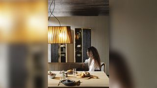 Frau sitzt unter Designer-Lampenschirm beim Frühstück am Holzesstisch