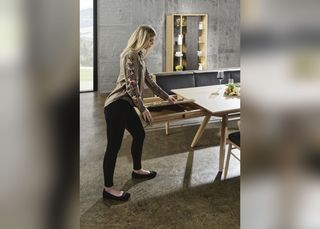 blonde Frau demonstriert den Ausziehmechanismus eines Vollholztisches